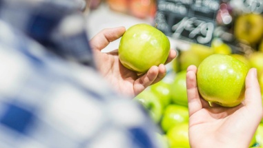 Close up of a man holding a green apple in each hand, trying to decide between them.