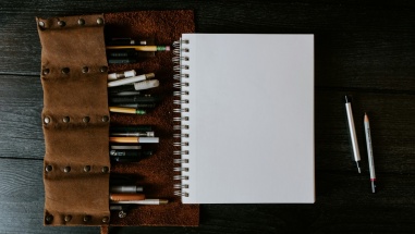 One notebook page with pencils and pens around it.
